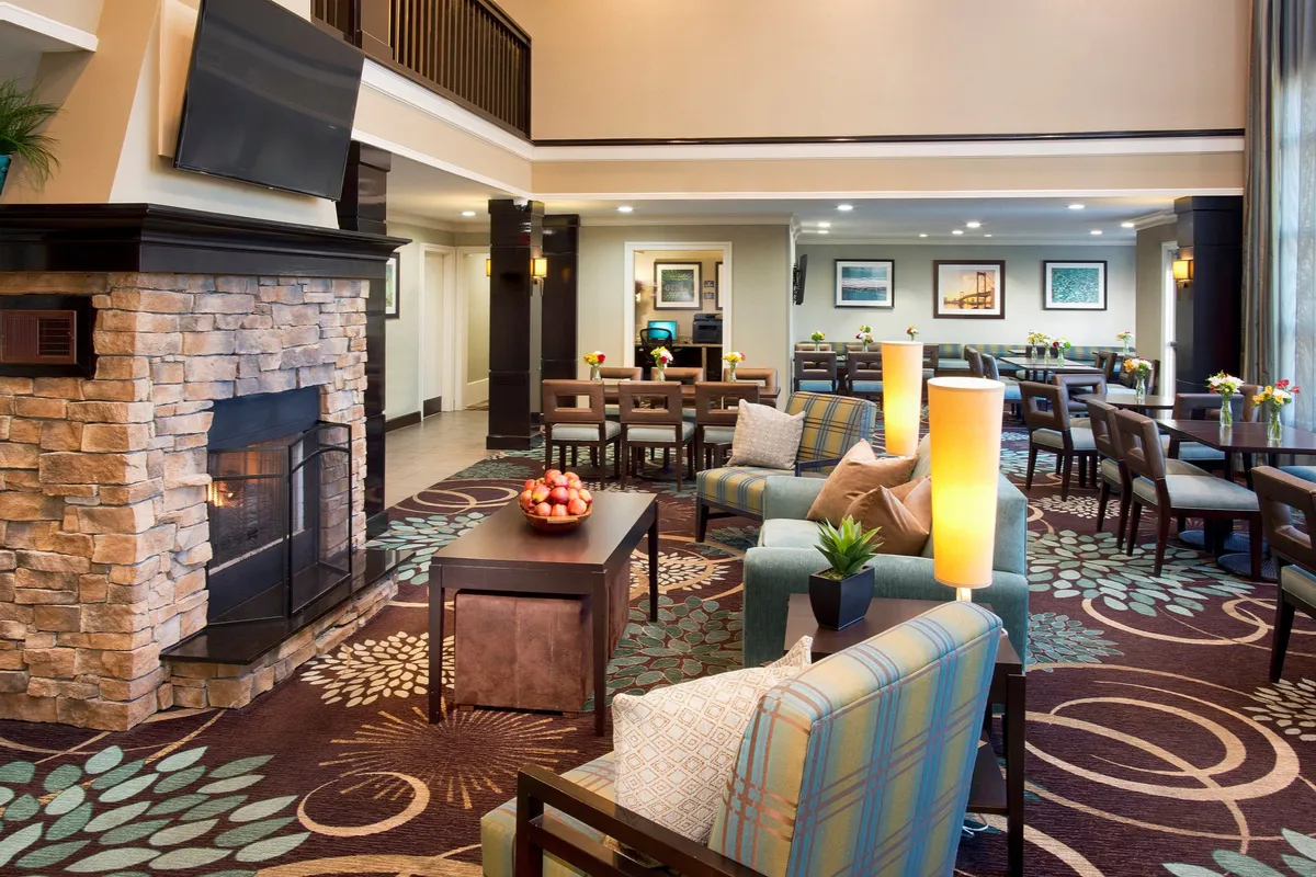 A spacious interior featuring a dining area adjacent to a comfortable seating area and fireplace, complemented by decorative artwork. The open layout fosters connection between kitchen, dining, and living spaces, illustrating the ease of socializing or enjoying meals together.