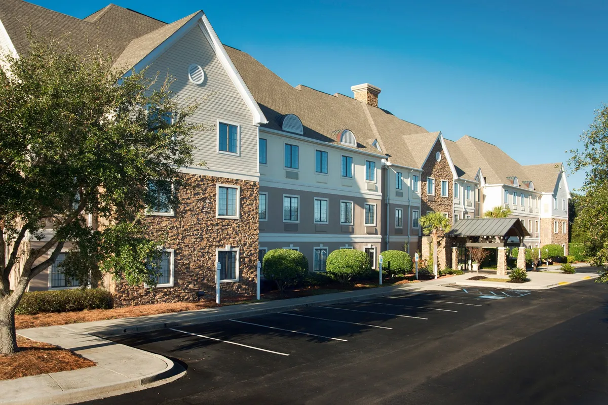 This image captures the main entrance of the property, featuring an inviting awning, landscaped bushes, and warm exterior textures. The scene conveys a welcoming atmosphere, highlighting easy access and a pleasant arrival experience for business travelers.