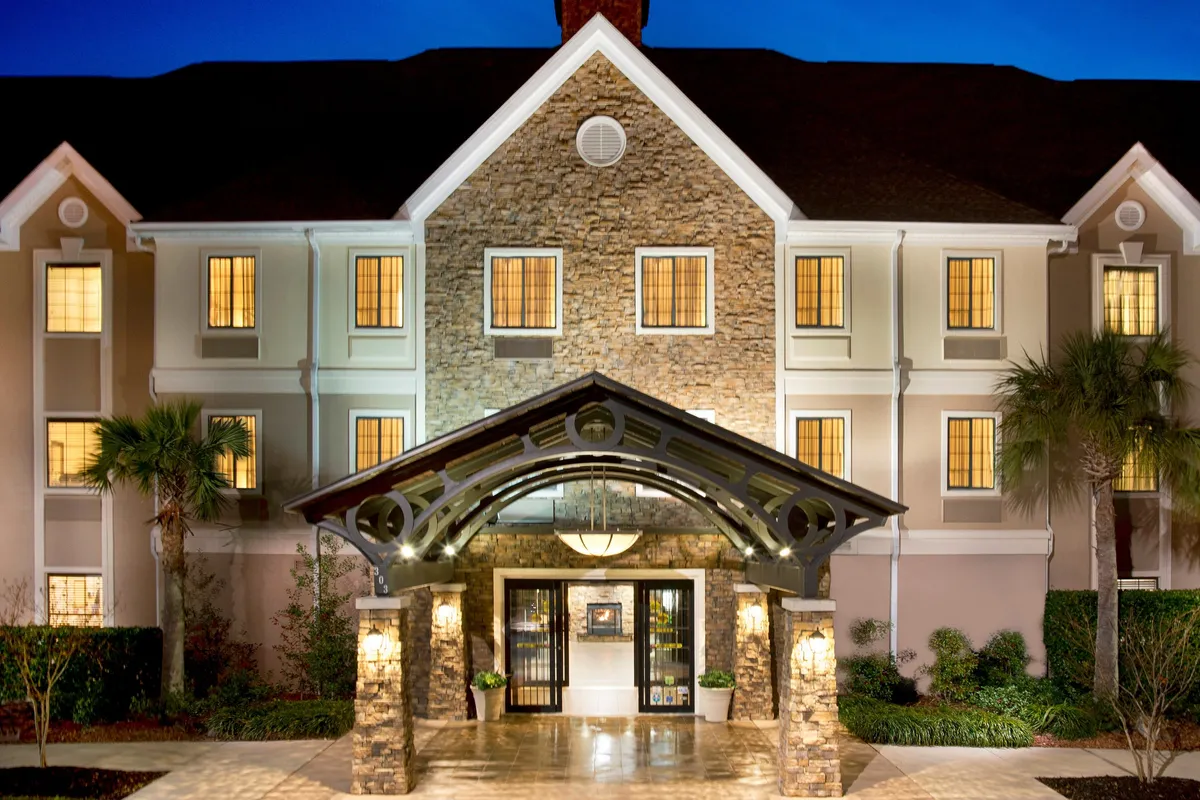 Showcasing the main entrance with a prominent arched awning and lush greenery, this image offers another inviting view of the property exterior. The facade's warmth suggests comfort and professionalism, complementing the section's message of productivity and hospitality.