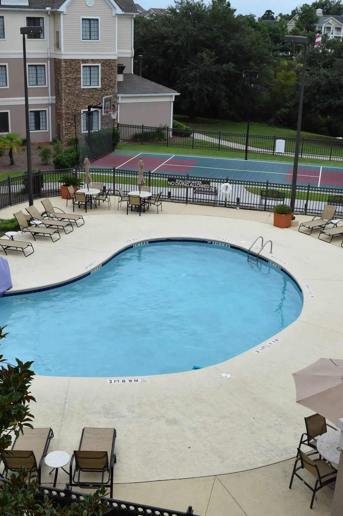This exterior shot captures the property's swimming pool, adjacent lounge chairs, and a tennis court in the background. The scene conveys opportunities for active recreation, social connection, and relaxation, all set within a leisurely, sunlit atmosphere.