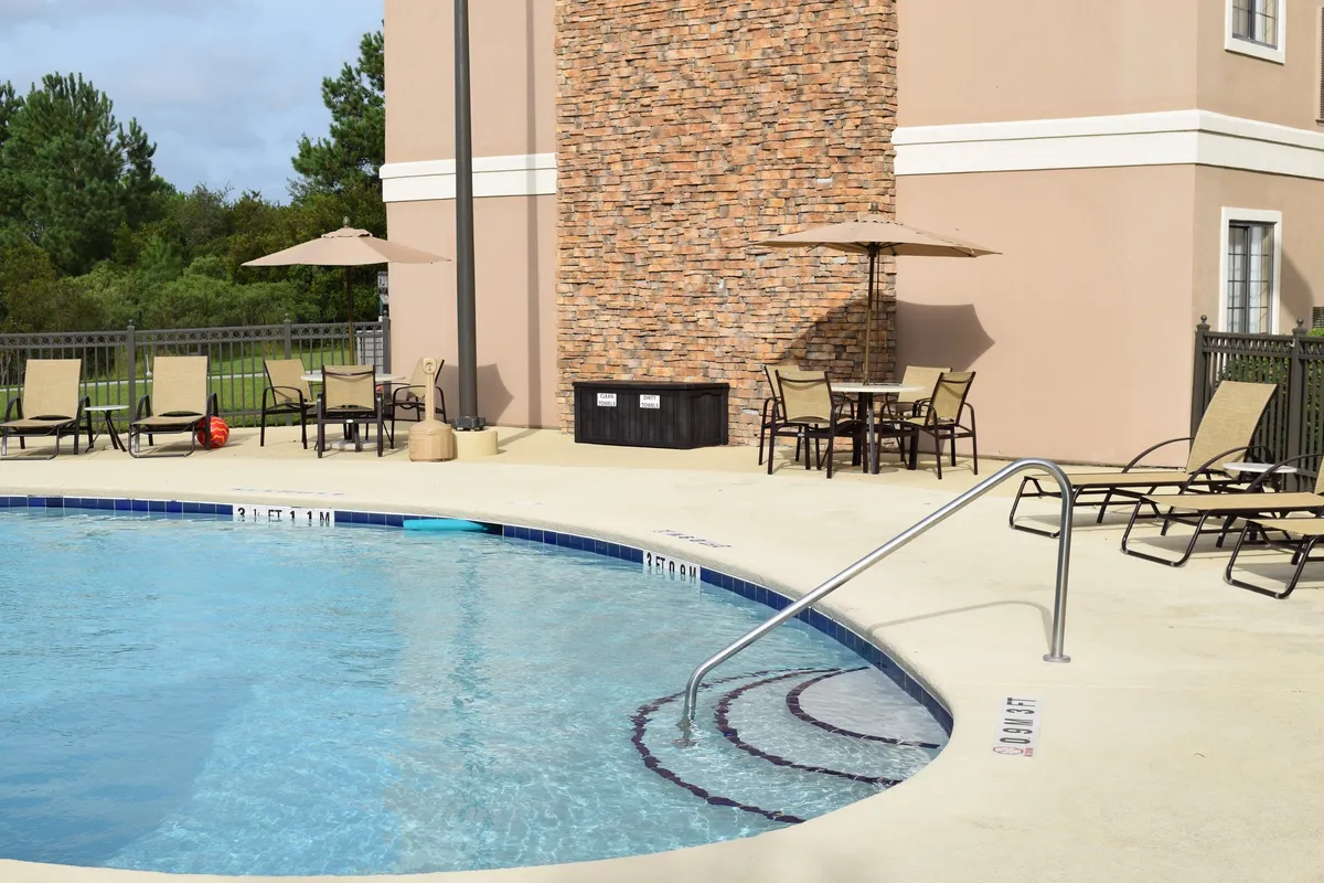 This exterior image features a tranquil swimming pool surrounded by a stone wall and lounge chairs shaded by umbrellas. The inviting setting is ideal for relaxation, socializing, or watching the sunset, with guests enjoying the outdoor amenities in a leisurely atmosphere.
