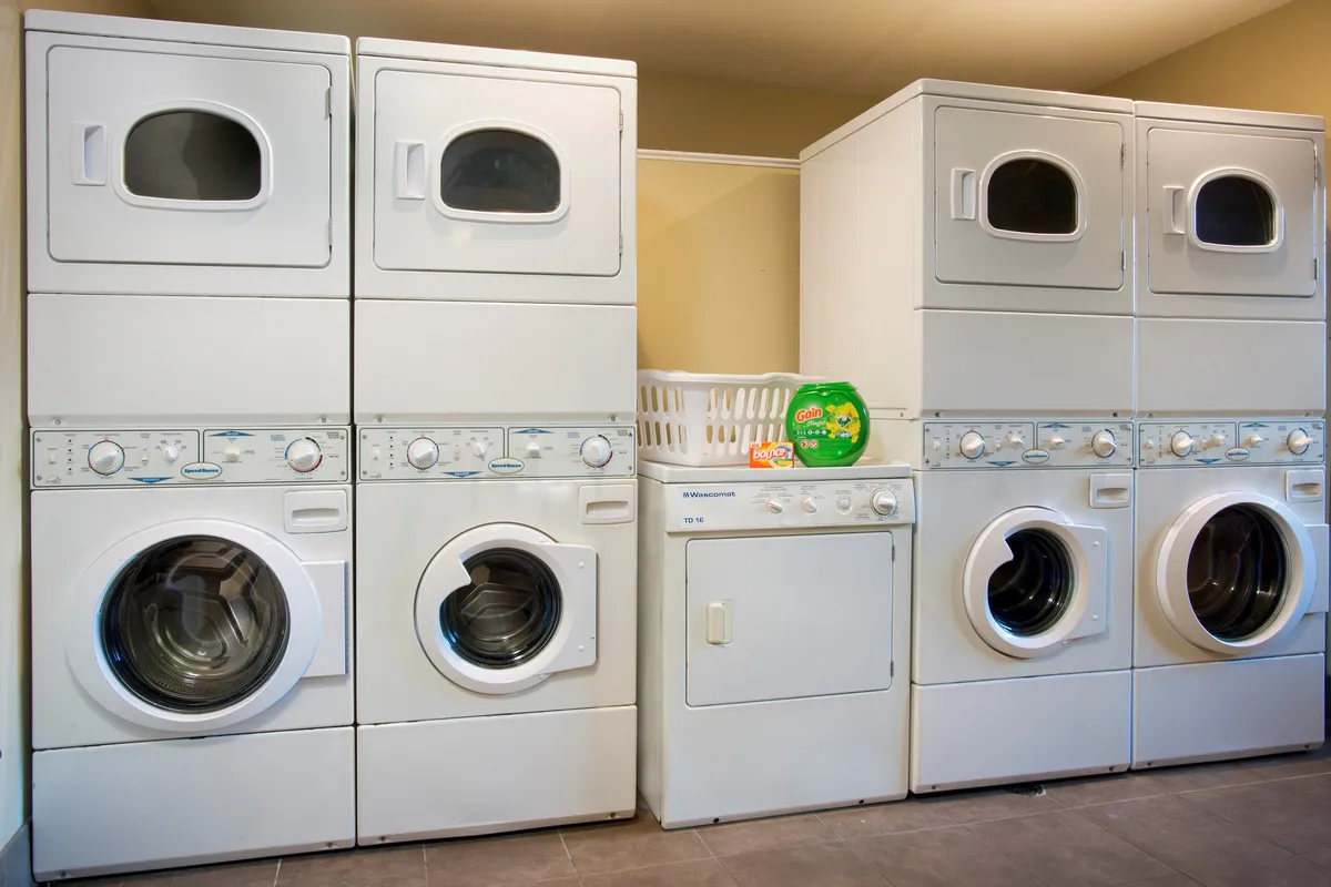 A tidy laundry area with stacked washer and dryer units, a laundry basket, and detergent neatly arranged. The space is clean and practical, emphasizing ease and self-sufficiency for guests.