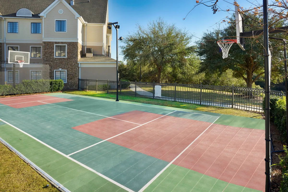 A playful exterior scene featuring a basketball court and hoop, with the property's building and lush greenery in the background. The court serves as a hub for friendly games, exercise, and family fun under the sun.