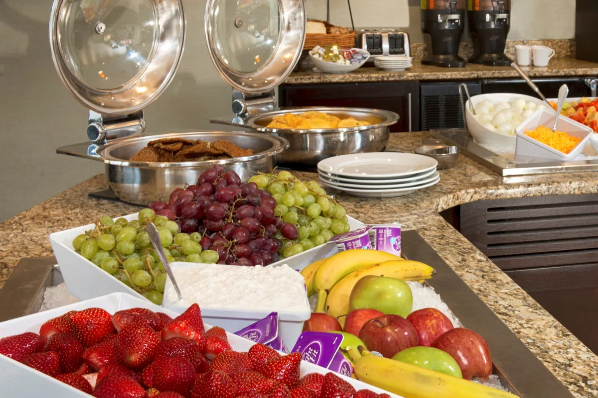 This image shows a bright breakfast area featuring fresh fruits, an inviting coffee station, and guests enjoying breakfast together in a cheerful, relaxed atmosphere. The space is open and appears easy to navigate, with seating arranged for comfort and accessibility.