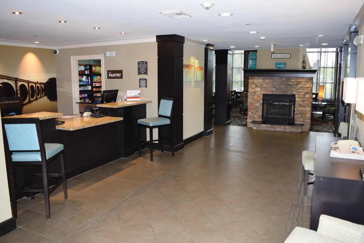The image features a welcoming reception area with a comfortable seating zone, a cozy fireplace, and a pantry for quick snacks. The overall ambiance is inviting, mirroring the hotel-style welcome and efficient check-in described in the section.